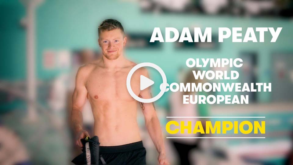 Professional swimmer Adam Peaty stood at the edge of a swimming pool 